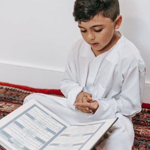A young boy dressed in white reads the Quran, symbolizing cultural and religious devotion.